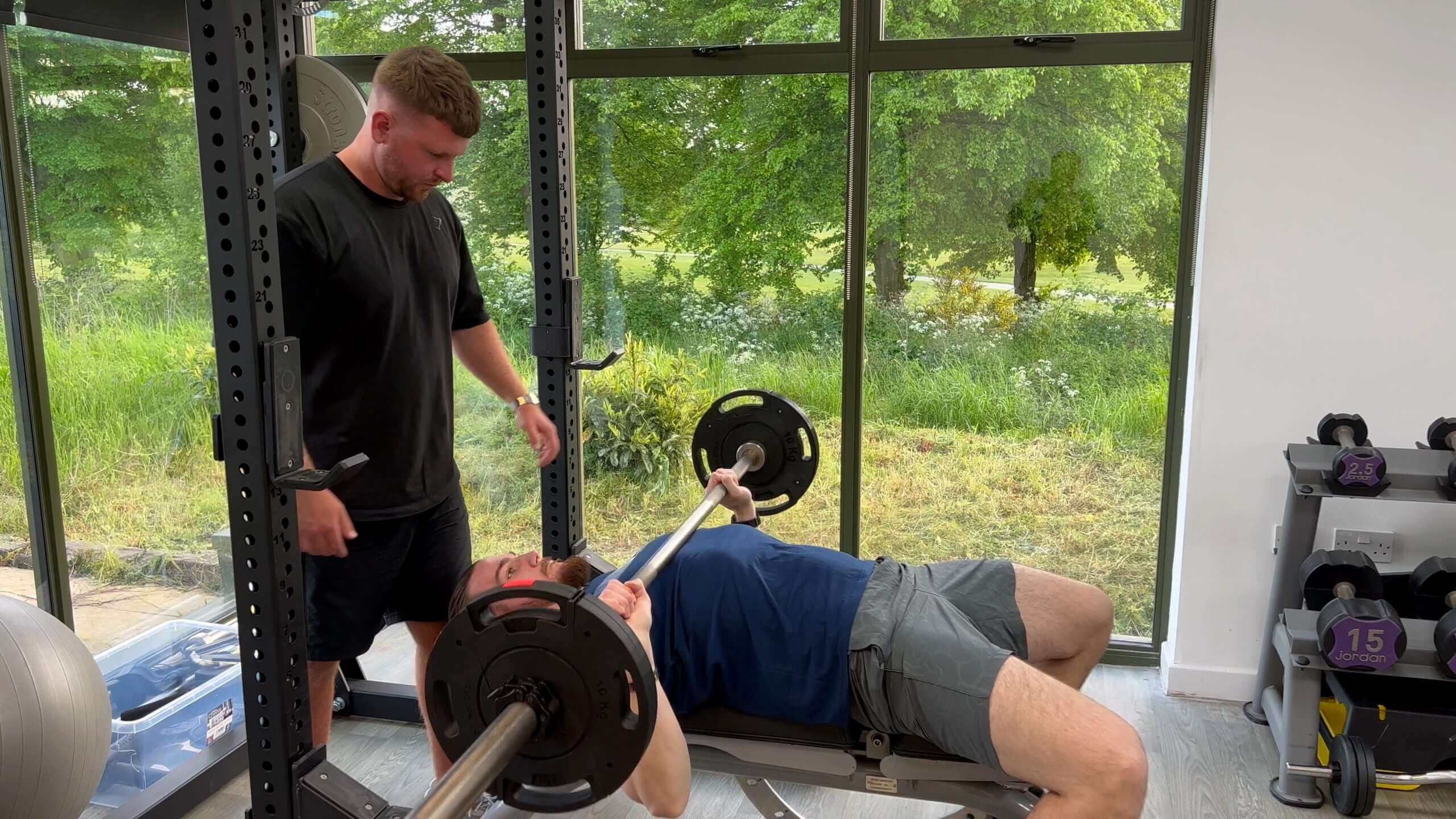 a man assisting another man during weight lifting exercises in a gym
